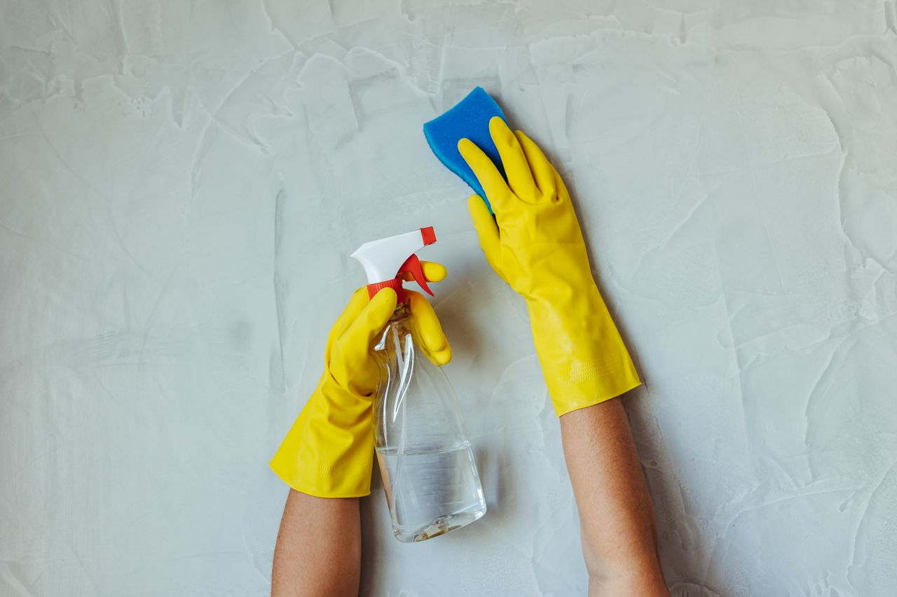 services-04 Gros plan sur des mains gantées de jaune nettoyant un mur avec un flacon pulvérisateur et une éponge.